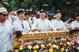 Illustration: Balinese musicians play a decorated traditional gamelan instrument during an outdoor cultural ceremony.