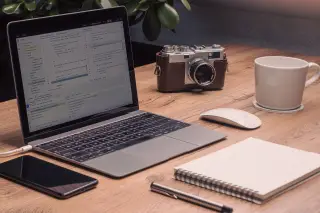 Illustration: A wooden desk with an open laptop, a vintage camera, a notebook, a pen, and a coffee mug.