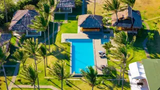 Illustration: Aerial view of tropical thatched-roof villas surrounding a swimming pool with palm trees.