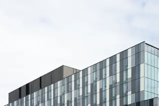 Illustration: Upper facade of a modern office building with geometric panels against an overcast sky.