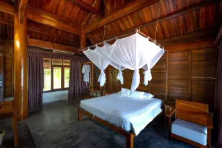 Illustration: A spacious wooden resort bedroom with a canopy bed draped in white netting.
