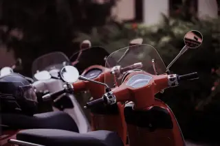 Illustration: A row of modern scooters parked outdoors with a helmet on the seat.