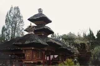 Illustration: Traditional Balinese shrine with tiered thatched roofs in a temple complex.