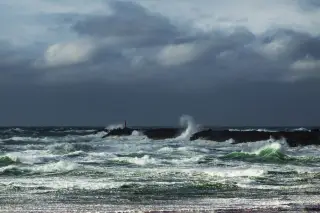 Illustration: Rough, white-capped sea waves crashing against a dark breakwater under a stormy sky.