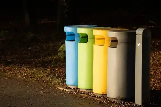 Illustration: Four colorful waste separation bins and a small post lined up along an outdoor path.