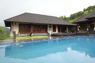 Illustration: A single-story villa with a tiled roof sits beside a bright blue swimming pool on a cloudy day.
