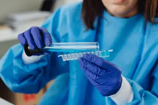 Illustration: A gloved laboratory worker transfers blue liquid into sample vials.