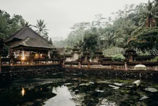 Illustration: A traditional Balinese water temple complex surrounded by a pond and tropical greenery.