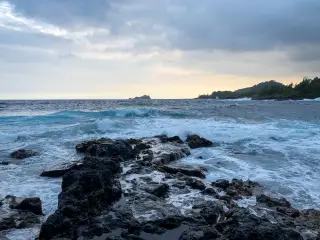 Illustration: Waves breaking over dark coastal rocks under a cloudy sky.