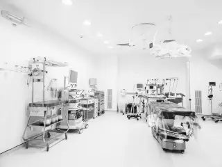 Illustration: An empty, brightly lit medical room with a surgical bed, infant warmer, and various medical equipment.