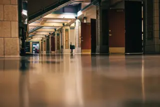 Illustration: An empty, quiet indoor hallway with polished floors and open wooden doors.