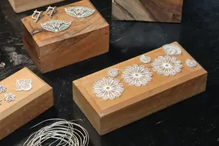 Illustration: Delicate silver filigree jewelry pieces arranged on wooden blocks on a workbench.