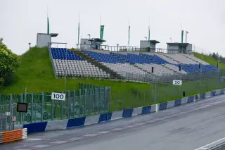 Illustration: An empty grandstand with blue and white seats alongside an asphalt racing circuit track.