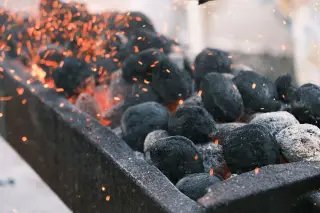 Illustration: Glowing charcoal briquettes with flying sparks in a grill trough.