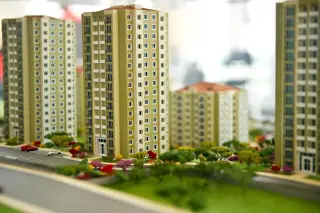 Illustration: A detailed architectural scale model of high-rise apartment buildings with miniature trees and parking spaces.