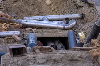 Illustration: Metal and plastic pipes laid inside an excavated trench for underground utility works.