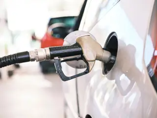 Illustration: A fuel pump nozzle inserted into the tank opening of a white car.