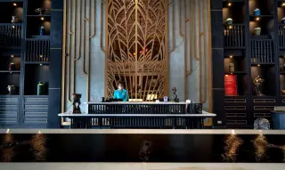 Illustration: A hotel receptionist wearing a face mask stands behind an ornate front desk in a luxury lobby.