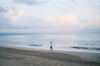 Illustration: A solitary person walks along a sandy beach near the ocean under a cloudy sky.