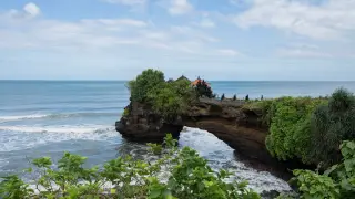 Illustration: A Balinese coastal cliff and sea arch with temple structures against ocean waves and cloudy sky.