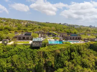 Illustration: Aerial view of a luxury cliffside resort with a swimming pool surrounded by green vegetation.