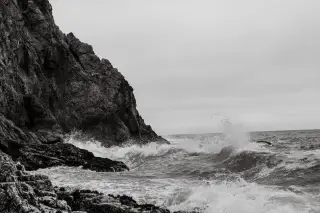 Illustration: Black and white photograph of rough sea waves crashing against a rocky cliff.