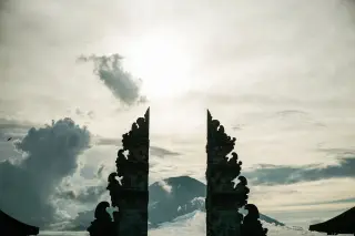 Illustration: A Balinese split gate silhouetted against a mountain and a cloudy sky.