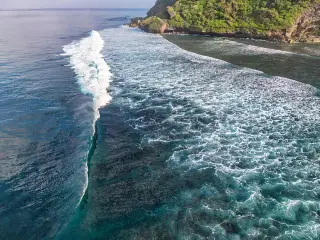 Illustration: Aerial view of ocean waves breaking near a rocky tropical coastline.