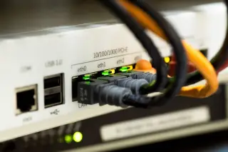 Illustration: Close-up of ethernet cables plugged into a network router with indicator lights glowing.