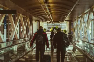 Illustration: Two people with luggage walking away down an airport walkway corridor.