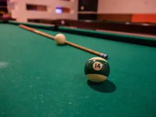 Illustration: A green number 14 ball, cue stick, and white cue ball on a green pool table.