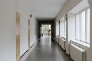 Illustration: An empty indoor hallway with doors on one side and windows with radiators on the other.