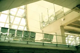 Illustration: Modern airport terminal interior with empty metal seats and glass architectural elements.