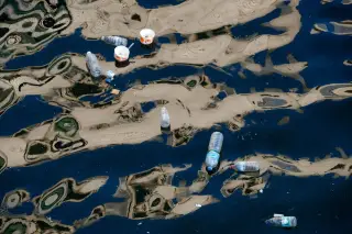 Illustration: Discarded plastic bottles and paper cups floating on rippling dark water with reflections.
