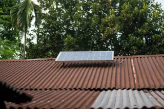 Illustration: A small solar panel mounted on a corrugated tin roof with trees in the background.