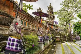 Illustration: Balinese stone statues with checked cloth and decorative umbrellas spouting water at a temple.
