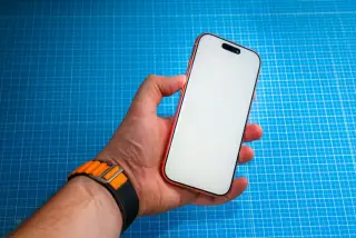 Illustration: A hand holding a modern smartphone with a blank white screen over a blue cutting mat.