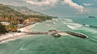 Illustration: An aerial view of a tropical coastal shoreline with resorts, palm trees, and ocean waves.