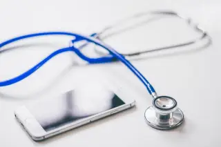 Illustration: A blue stethoscope lying next to a white smartphone on a desk.