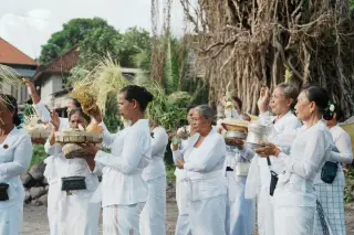 Illustration: Balinese women dressed in white hold ceremonial offerings outdoors during a traditional ritual.