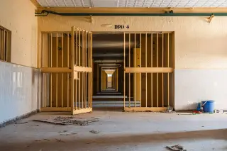 Illustration: An empty, dilapidated corridor seen through open yellow prison-like barred gates.