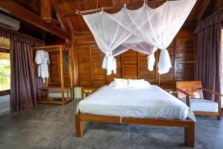 Illustration: A wooden resort bedroom featuring a canopy bed with a white mosquito net.