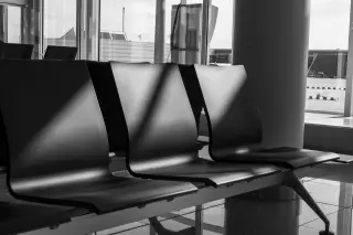 Illustration: Black and white view of empty chairs in an airport terminal next to large windows.