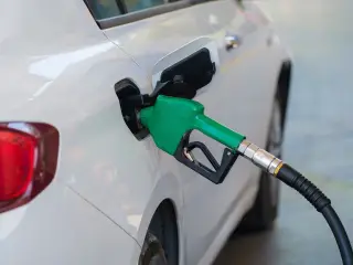 Illustration: A green fuel nozzle inserted into a white car's fuel tank at a station.