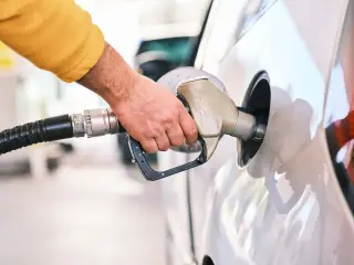 Illustration: A close-up of a person's hand inserting a fuel nozzle into a white car's tank.