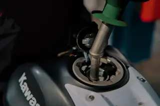 Illustration: Close-up of a fuel nozzle inserted into a motorcycle gas tank.