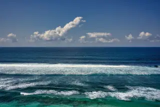 Illustration: Rolling ocean waves under a blue sky with scattered clouds.