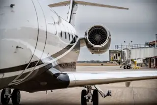 Illustration: Close-up of a jet aircraft parked on an airport tarmac near a boarding bridge.