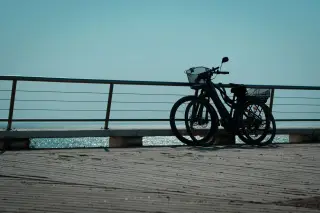 Illustration: Two bicycles parked by a railing on a seaside boardwalk under a clear sky.