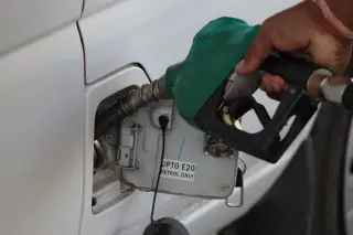 Illustration: Close-up of a hand inserting a green fuel nozzle into a white car's tank.